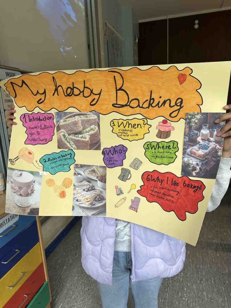 Ein Kind hält ein großes, farbenfroh gestaltetes Plakat mit dem Titel „My hobby Baking“ in den Händen. Das Plakat enthält Texte, Zeichnungen und Fotos rund ums Thema Backen.