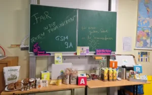 Verschiedene Fairtrade-Produkte sind auf zwei Tischen angerichtet zu einem Frühstücksbuffet vor einer grünen Wandtafel.