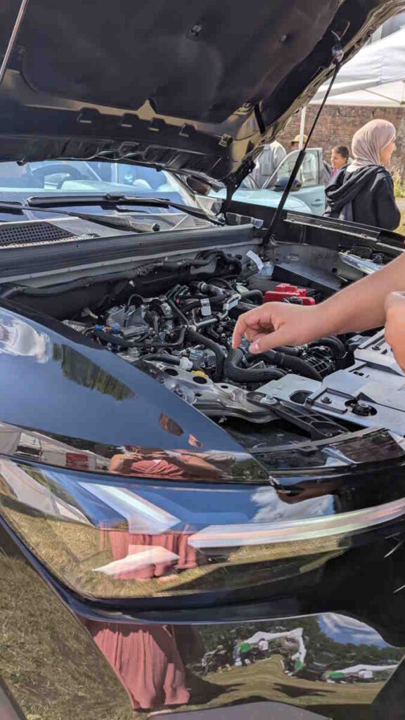Ein Schüler arbeitet unter einer geöffneten Motorhaube an einem Schlauch.