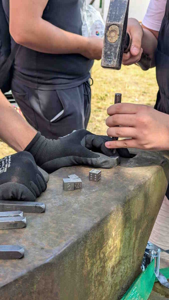 Ein Schüler bearbeitet mit dem Hammer ein Werkstück aus Eisen auf einem Amboss.