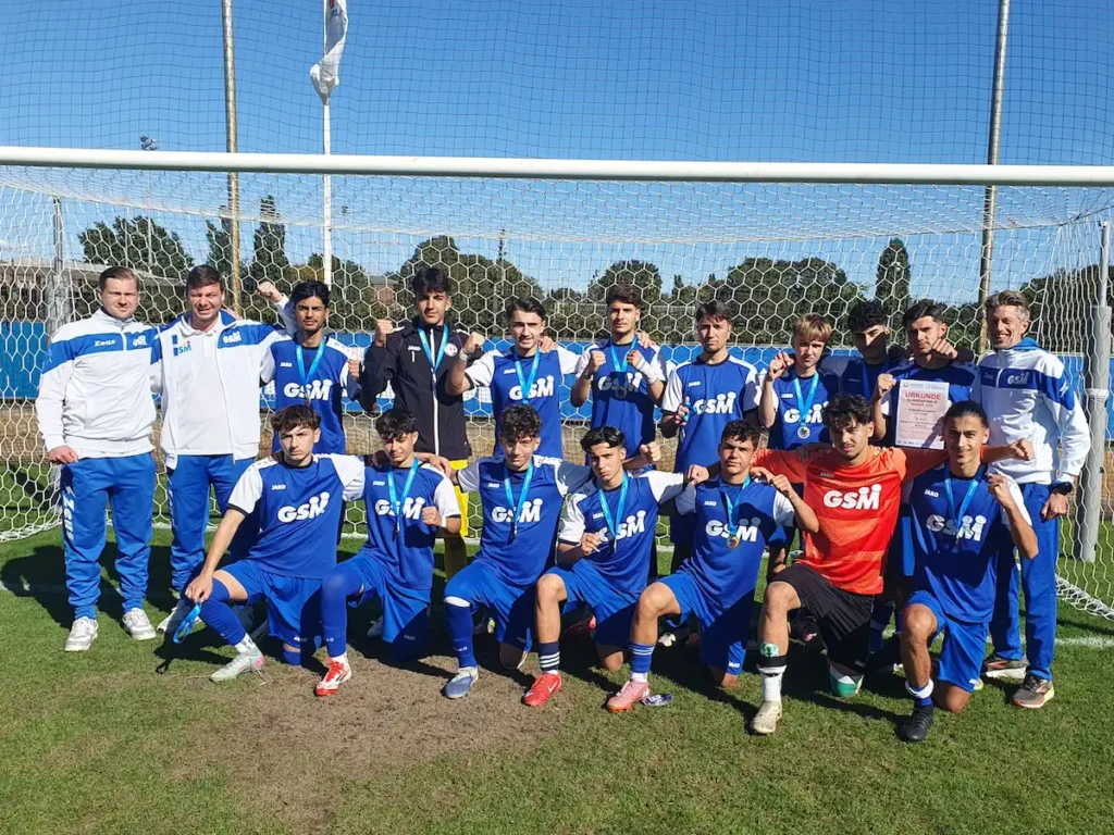 Mannschaftsbild der U18-Jungen-Fußball-Mannschaft der Gesamtschule Meiderich nach dem Finale in Berlin. Die Schüler und ihre Lehrer haben sich zum Foto in einem Tor positioniert und tragen um den Hals die Medaillen für den zweiten Platz.
