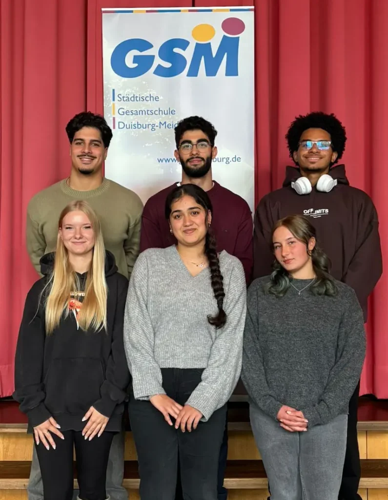 3 Schülerinnen und 3 Schüler stehen vor einem Plakat mit dem Logo der Gesamtschule Meiderich. Sie bilden die Schülervertretung.