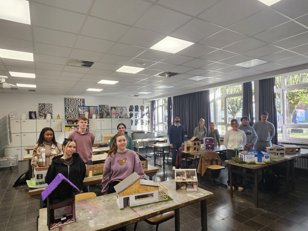 Schüler der Jahrgangsstufe Q2 stehen im Kunstraum er Schule hinter ihren Kunstwerken.