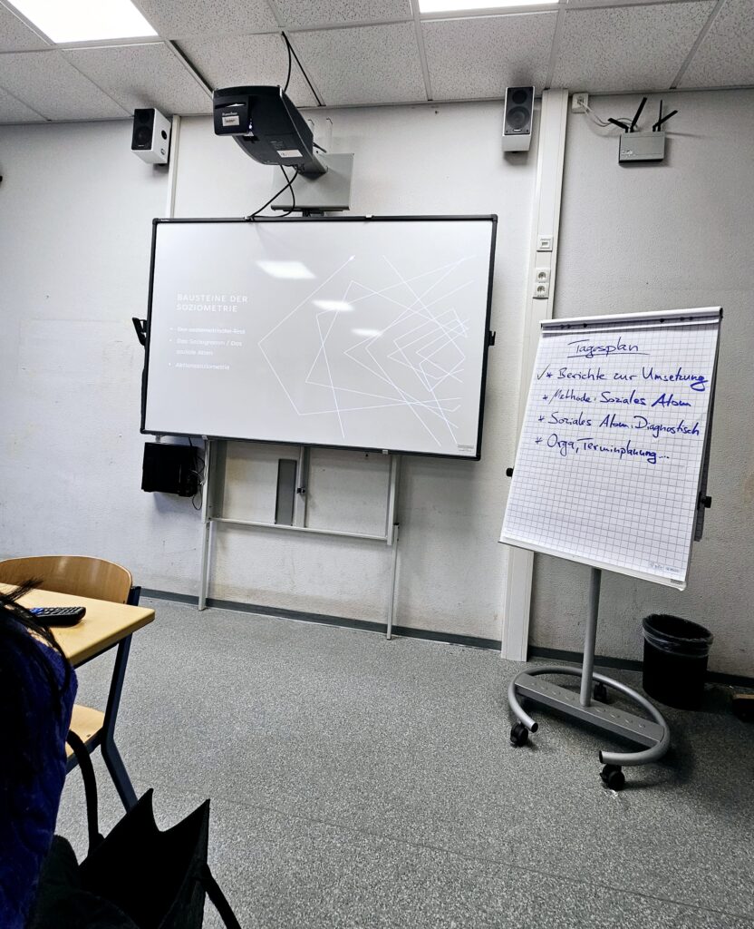 Szene aus einem Seminar. Man sieht ein Whiteboard und eine Flipchart rechts daneben.