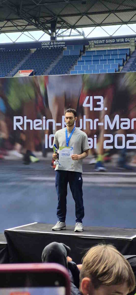Mohammad Alhariri als Sieger in seiner Altersklasse auf dem Siegerpodest mit Trophäe und Urkunde in der Hand
