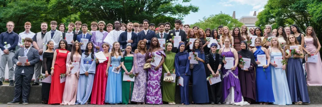 Gruppenbild der Abiturienten und Abiturientinnen der Gesamtschule Meiderich nach der Zeugnisverleihung. Die Schüler halten ihre Zeugnisse und eine Rose in der Hand und schauen in die Kamera.